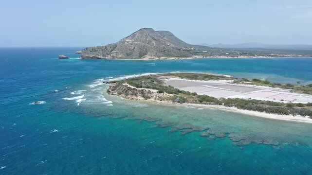 Scenic aerial view of coastal island with salt pans and mountain in distance.