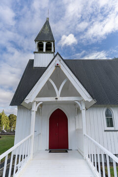 St Catherine's Anglican Church with red doors and bell tower under a cloudy sky in Okaihau, New Zealand