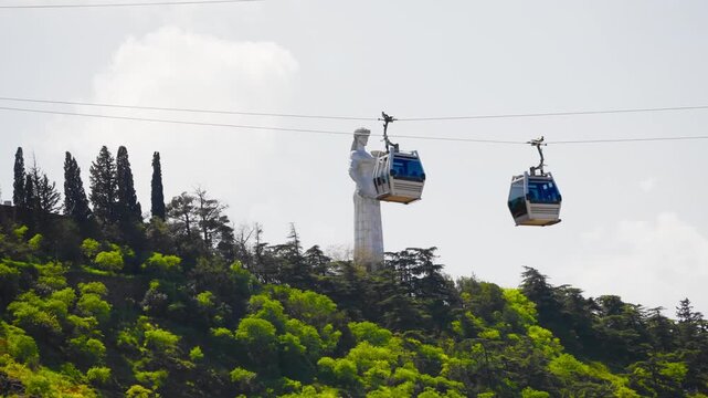 Cable car cabins passing the Kartlis Deda monument, the Mother of Georgia statue on the Sololaki ridge above Tbilisi.