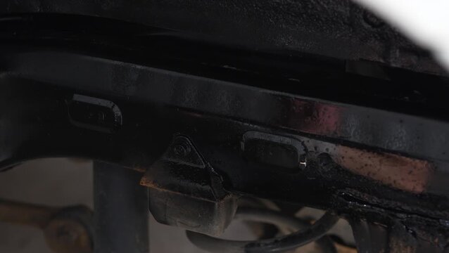 Man spraying black protective anti-corrosion coating onto car chassis part.