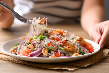 Eating Thai spicy glass noodle salad with minced pork and shrimp (Yum Woon Sen) on a white plate © nungning20