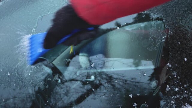 Hand removing ice and frost from a car window on a cold winter day. Winter car care, windshield maintenance, safe driving preparation, and keeping a vehicle in good condition concept.