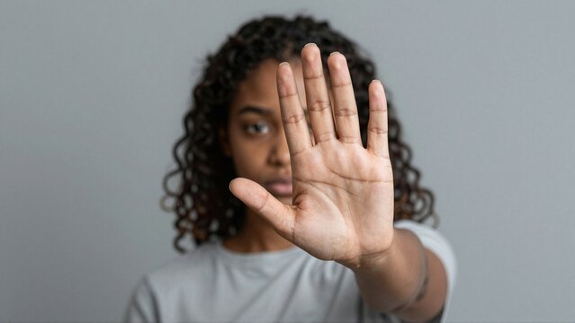 Black woman making assertive stop gesture with outstretched palm against gray background