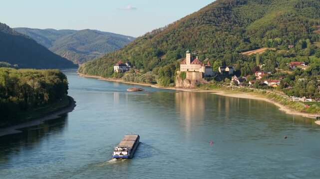 Sch&ouml;nb&uuml;hel Castle above the Danube River, with a river barge sailing through the low water level,  Lower Austria, Wachau Valley.