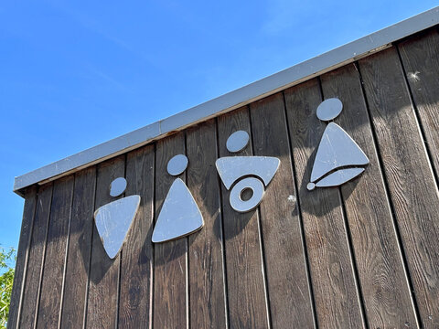 Metal pictograms marking public restroom facilities are displayed on the wooden exterior wall of a public toilet building in Rewa, Poland - August 15, 2026