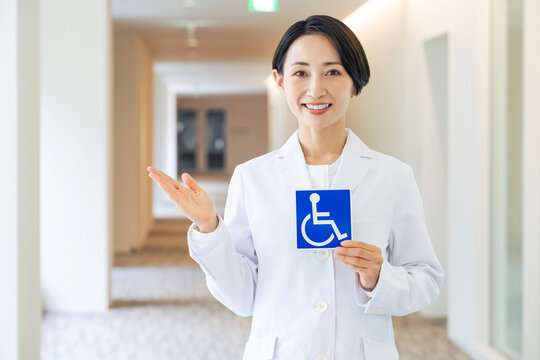 車いすマークを持つ白衣の女性。医師、介護、福祉、病院、支援、サポート、サービス、高齢者、障害者、医療