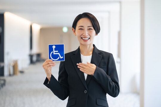 車いすマークを持つ女性。障害者、高齢者、バリアフリー、介護、福祉、安全、安心、思いやり、駐車場、施設