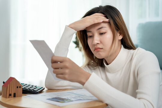 Debt house, Stressed and headache asian woman with large bills or invoices no money to pay, shortage, Financial problems, mortgage, loan, bankruptcy, bankrupt, poor, empty wallet, overdue
