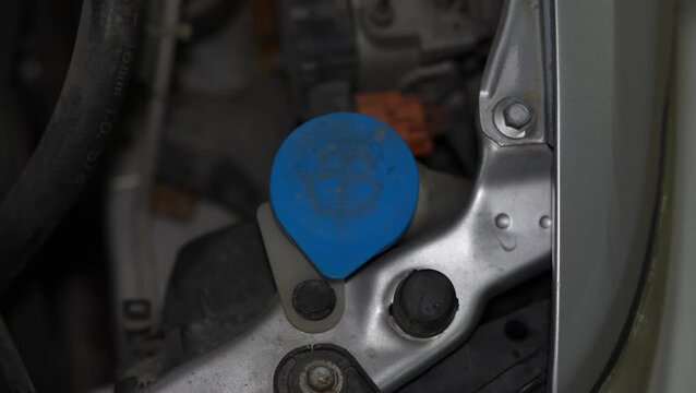 Blue plastic windshield washer fluid reservoir cap in car engine bay.