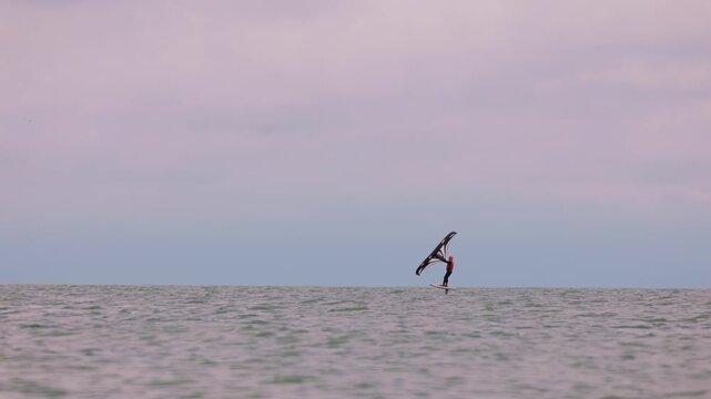 An athlete standing on the board holds on to the wing, in which the wind creates thrust in slow motion. Wingfoil board where a surfer glides through the water on a hydrofoil board..