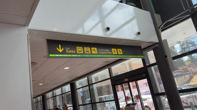 A modern airport concourse with a prominent black overhead sign, featuring directions and services