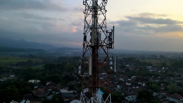 Aerial Scenery Footage of Radio Masts and Communication Equipment Mounted on a Large Telecommunication Tower Rises Above a Peaceful Countryside Village During Dawn in Kedungbanteng, Indonesia.