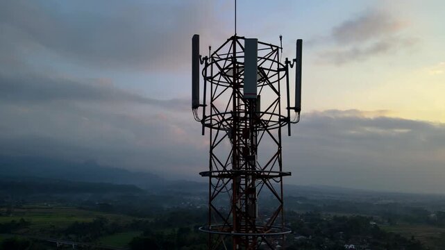 Aerial Scenery Footage of Radio Masts and Communication Equipment Mounted on a Large Telecommunication Tower Rises Above a Peaceful Countryside Village During Dawn in Kedungbanteng, Indonesia.