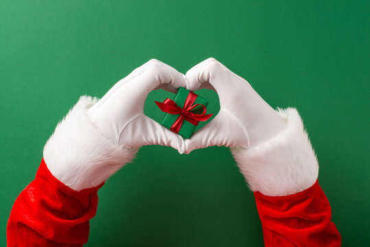 Merry Christmas and Happy New Year from Santa Claus holding a small gift heart with red ribbon