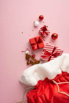 Merry Christmas happy New Year Santa Claus red stocking with wrapped present and festive ornament on vertical pastel pink background