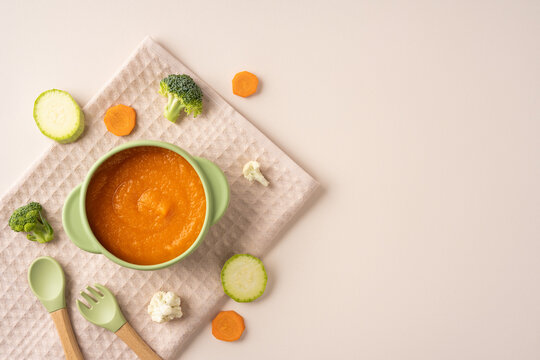 Baby's first feeding with healthy carrot puree in green bowl and utensils on light beige background