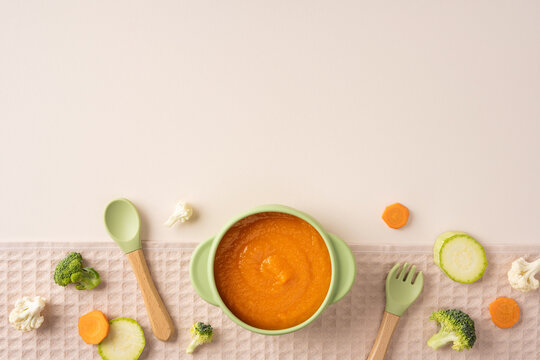 Baby's first feeding with homemade carrot puree in a green bowl and wooden spoon on textile light beige background