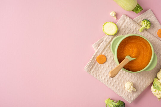Baby's first feeding with healthy vegetable puree in a bowl and wooden spoon on pastel pink background