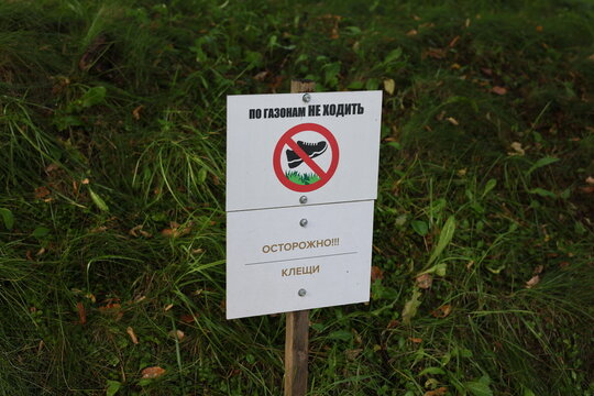 Safety signs warning visitors to keep off the grass and beware of ticks, placed beside a green lawn