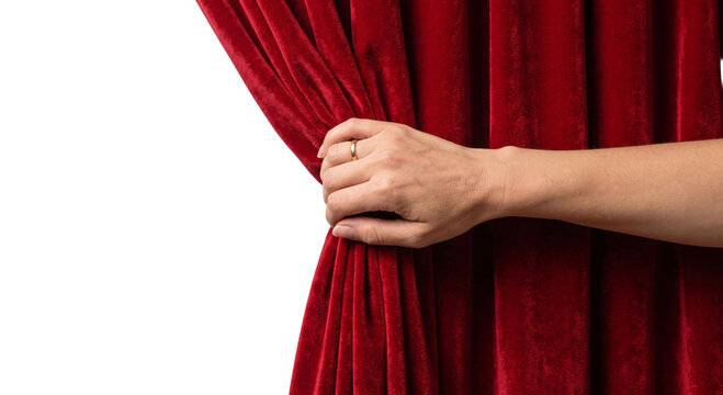 Hand pulling open a rich red velvet theater curtain to reveal a stage