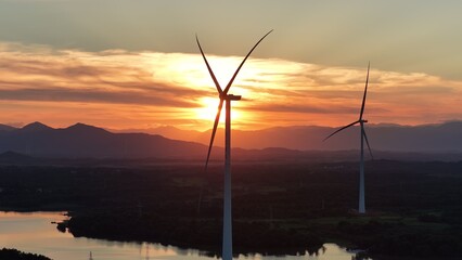 Obraz premium Wind turbines silhouetted against sunset sky over water