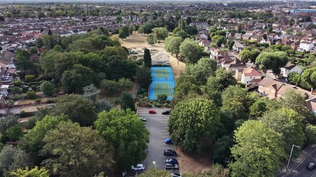 4K UHD cinematic drone tracking shot descending and flying forward past two newly renovated tennis courts, transitioning to reveal a beautiful kids' playground at Raphael Park, Romford, England