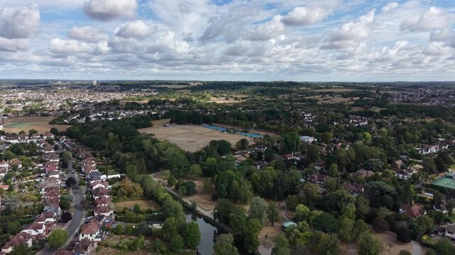 4K UHD cinematic high-altitude drone push-in shot over Raphael Park, Romford, England. Scenic wide view featuring a traditional cricket field in the background