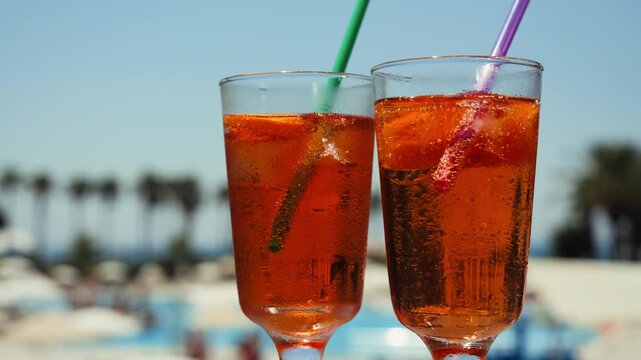 Two Aperol spritz cocktails with ice and orange garnish served outdoors in a sunny summer setting. Refreshing Italian-style drink for vacation, leisure, bar and hospitality concepts. High quality 4k