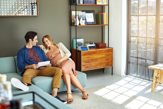 Happy, couple and pregnant woman in home with tablet, internet connection and research for baby name. People, smile and relax in lounge with relationship, pregnancy and tech for family planning.