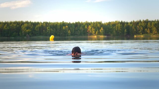 Hispanic guy swimming and diving, submerging from the clear blue water lake during golden hour.