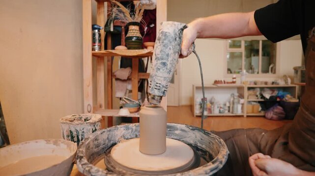 A handmade clay vase is carefully dried with a hair dryer during the pottery process, capturing a practical stage of ceramic making in an artisan studio.