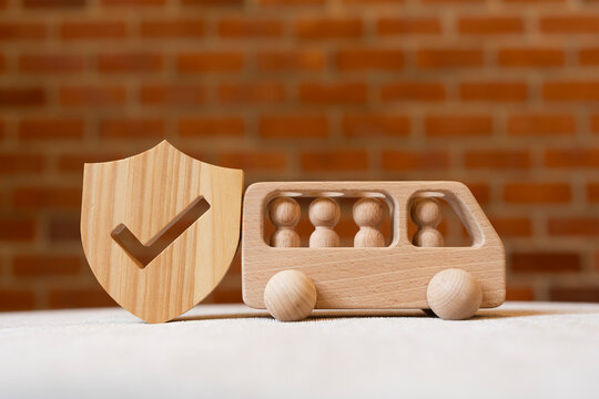 Passenger transport and vehicle safety concept with wooden toy bus carrying people figures beside shield with checkmark on table for public transit insurance and travel protection.