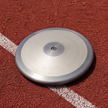 Discus throwing disc on red athletic track with white line