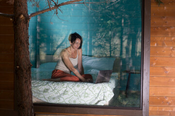 Fototapeta premium Mindfulness and feel-good moments. lifestyle portrait smiling middle aged woman works on a laptop while sitting on the threshold in a country house in the forest. work-life balance. remote work.