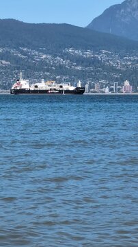 Pacific Ocean navigation &ndash; a cargo ship arrives to the Port of Vancouver against a beautiful mountains and blue sky. Wide shot, real-time footage. - Vancouver, BC, Canada - 07.28.2025