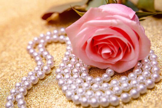 Pink rose and pearl necklace on a shiny gold background
