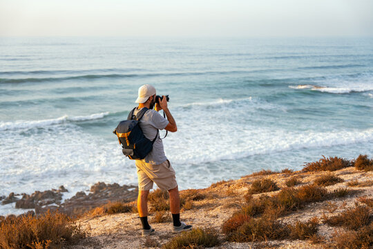 Man with backpack photographs the ocean from a cliff