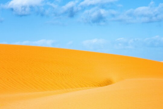 Bright orange Sahara desert sand dune against blue sky