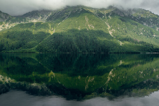 Morskie Oko lake reflects lush green mountains and cloudy sky in