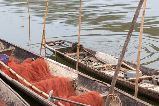 Traditional wooden fishing boats with red mesh nets moored along the riverbank in rural Asia.