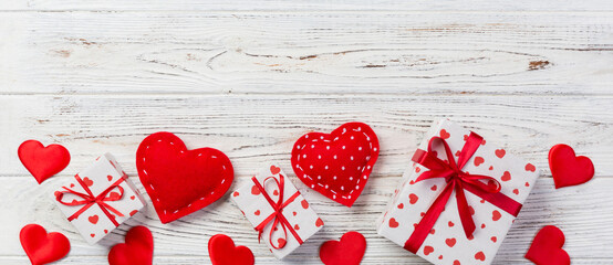 Fototapeta premium Valentine or other holiday handmade present in paper with red hearts and gifts box in holiday wrapper. Present box of gift on white wooden table top view with copy space, empty space for design