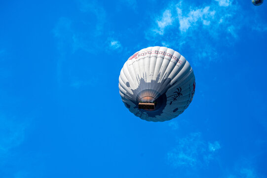 White hot-air balloon from Kaya Balloons photographed from directly below against a brilliant blue sky; the allure of hot-air ballooning; Cappadocia, Nevşehir, T&uuml;rkiye 28.3.25