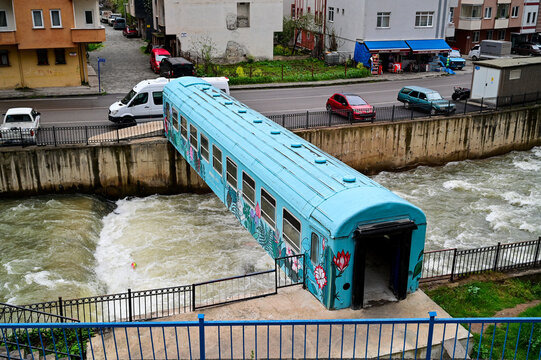 Blue, colorfully painted train carriage serving as a pedestrian bridge over a rushing river in the town center of Ma&ccedil;ka, Trabzon Province, Black Sea region, T&uuml;rkiye 29.3.25