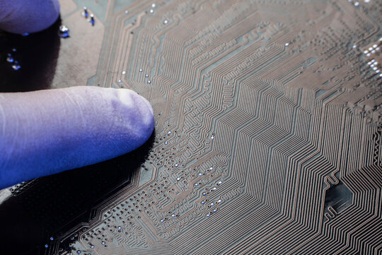 Scientist finger in protective glove inspecting complex copper traces on an artificial intelligence printed circuit board.