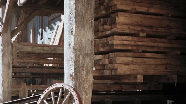 A lumber yard displays a wooden structure with several stacks of timber in the background. Natural light shines through, showing the textures of the wood.