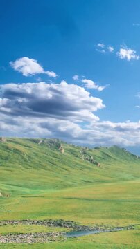 Time-lapse of drifting white clouds over lush green meadows and rolling hills under a vivid blue sky