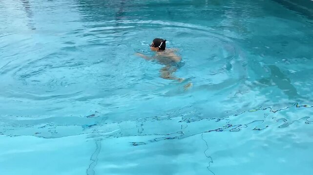 Boy diving under water to retrieve blue flipper from pool bottom.