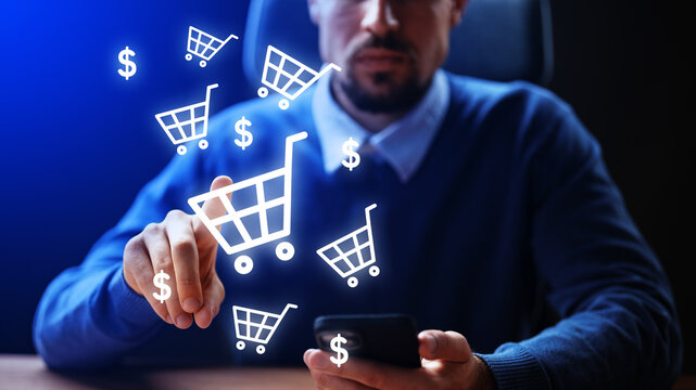 Man using smartphone for online shopping in a dark room with shopping cart icons