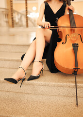 Elegant female cellist in a black evening dress holding a cello and bow. Classical music concept for concerts, orchestras, music education, cultural events and performing arts. © Aigul Sabirova