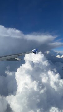Airplane wing gliding through fluffy white clouds against a bright blue sky, showcasing the serene beauty of high-altitude travel and the vastness of the atmosphere